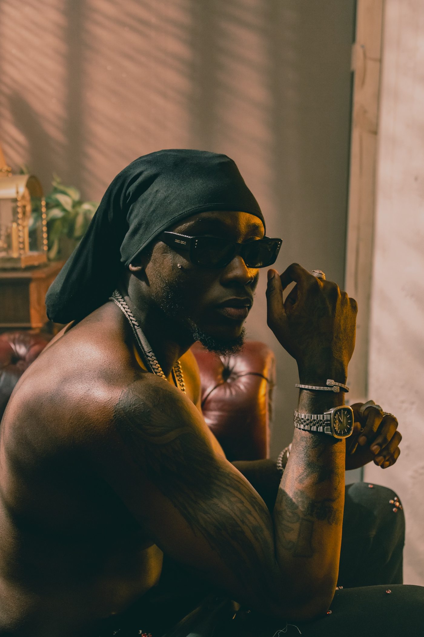 Portrait de profil, lunettes noires, main près du visage, montre et bracelets en évidence
