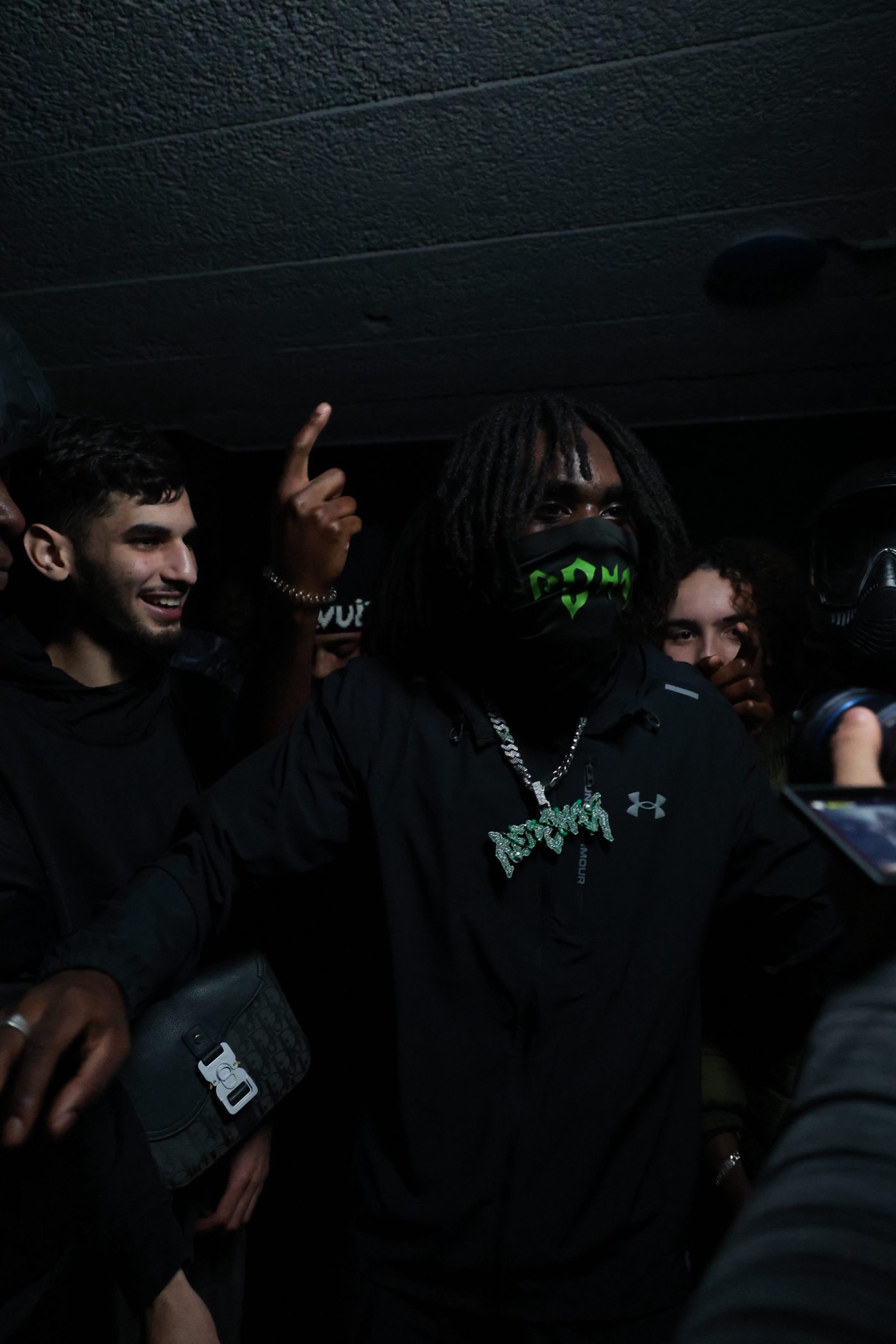 Homme aux locks, masque vert, le bras levé sous un plafond bas, équipe souriante