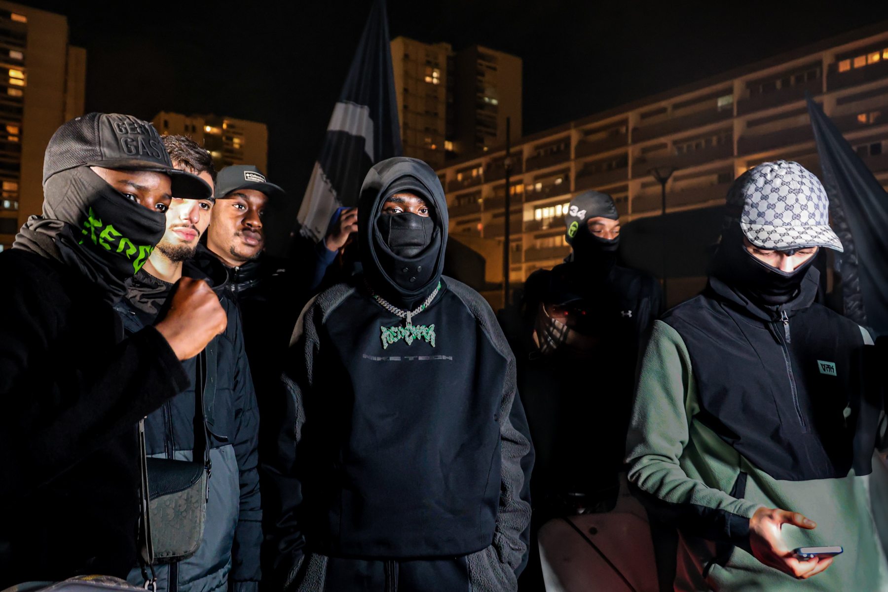Kerchak au centre de son équipe masquée, de nuit devant une barre d'immeubles