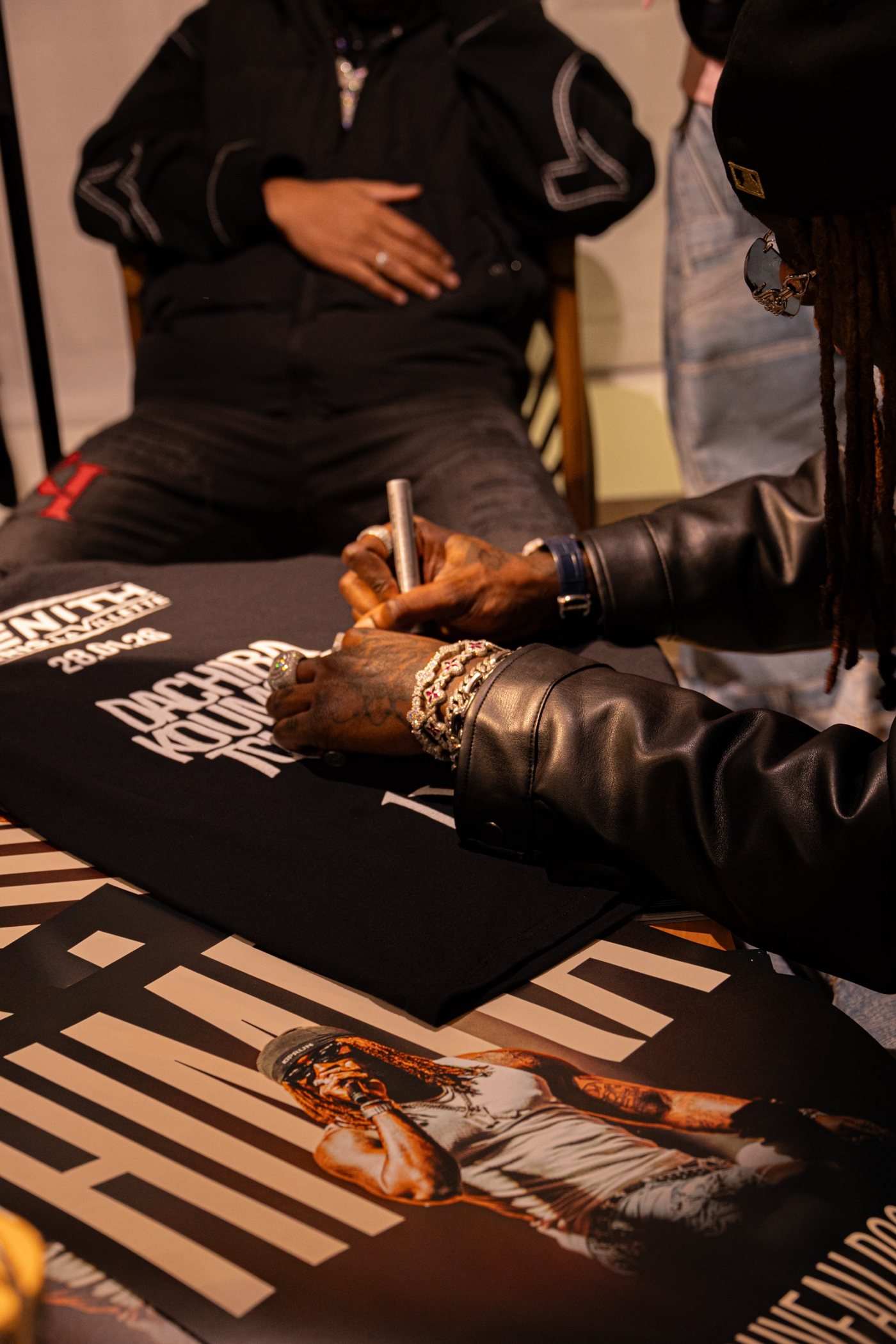 Dédicace : les mains baguées de l'artiste signent un t-shirt, affiche en bas