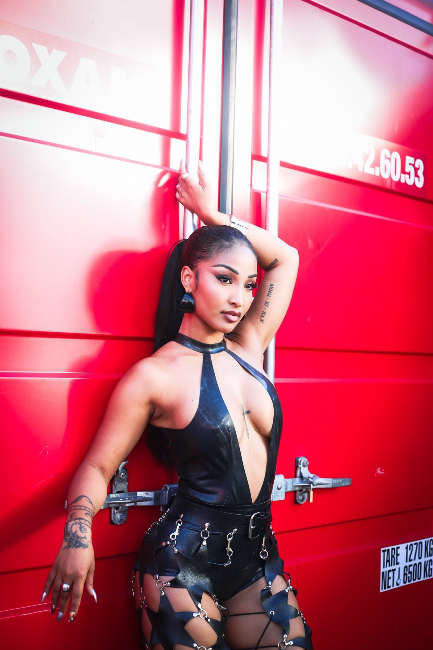 Portrait de mode devant un conteneur rouge, tenue noire en latex, bras levé