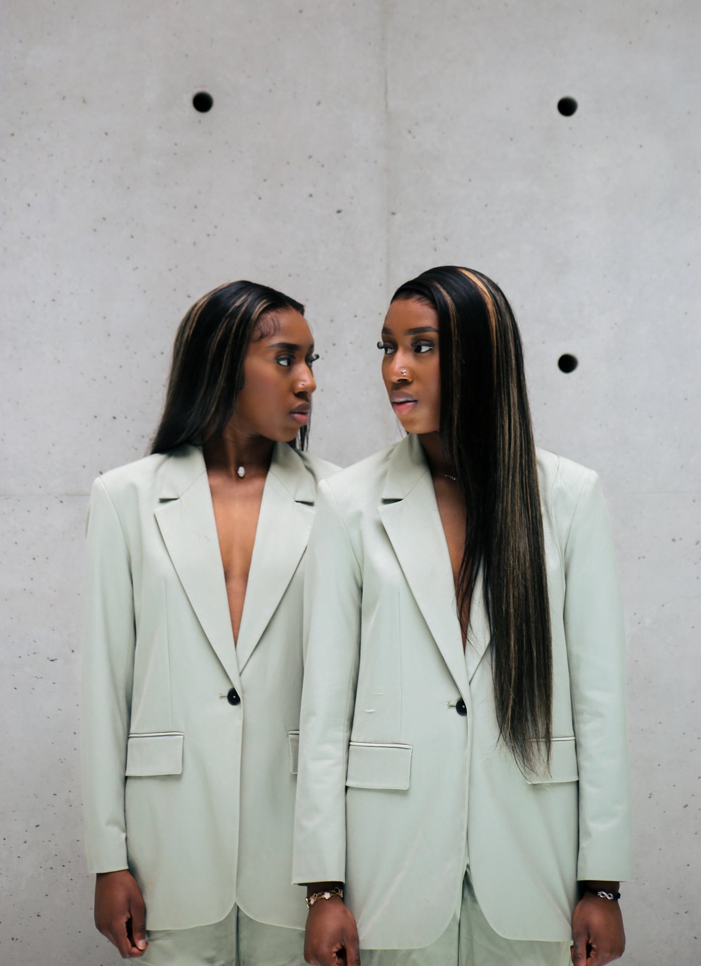 Deux jumelles en blazers vert sauge face à un mur de béton