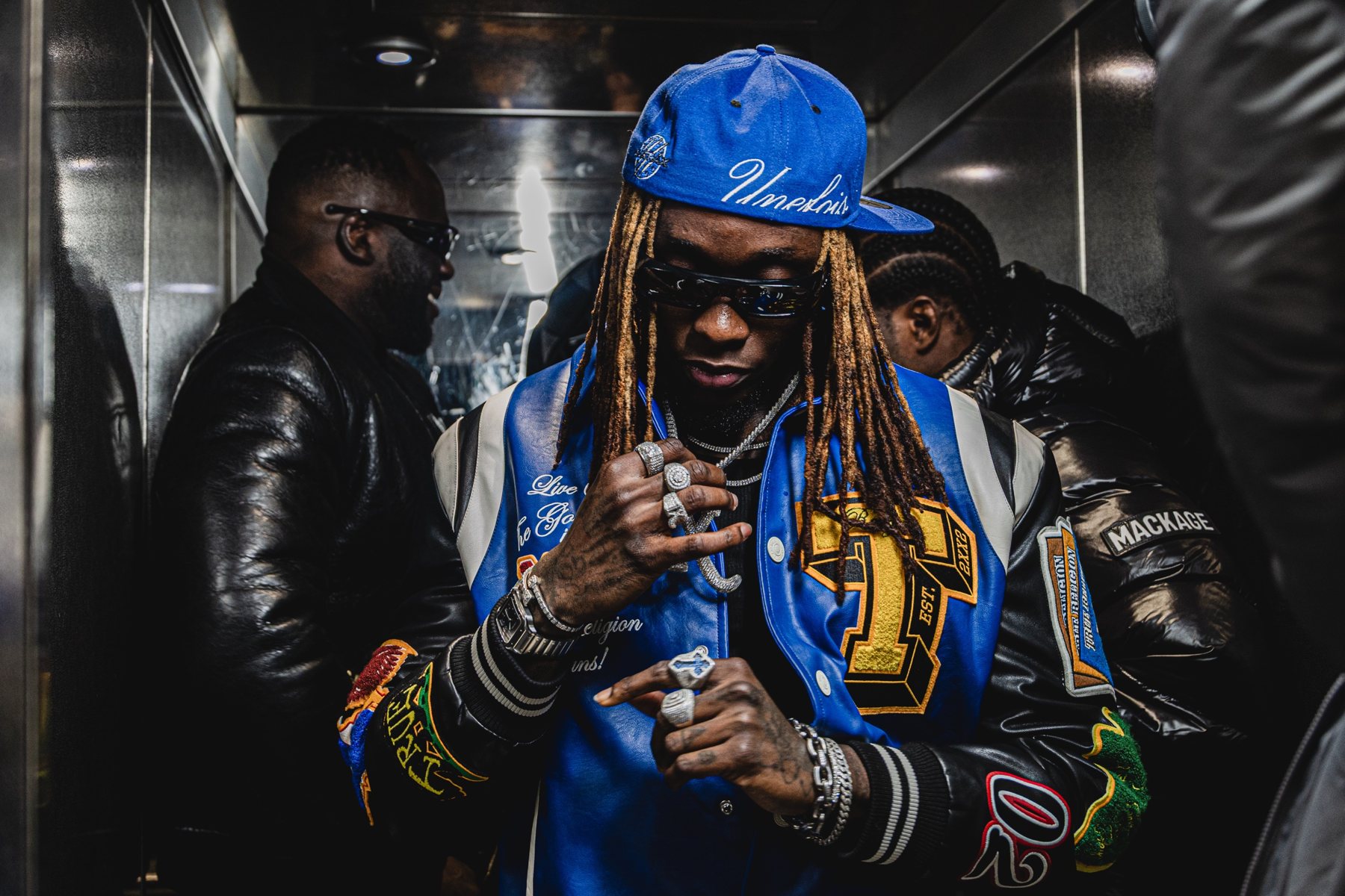 Artiste en casquette bleue et veste universitaire, bagues aux doigts