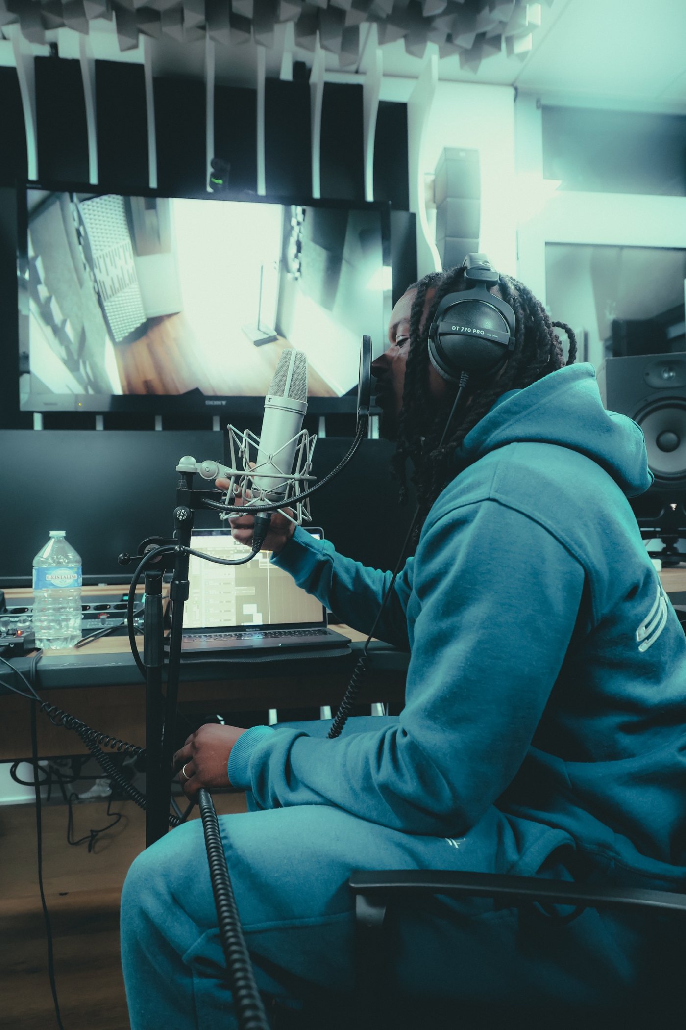 Studio : artiste au micro, casque sur les oreilles, console et écrans derrière lui