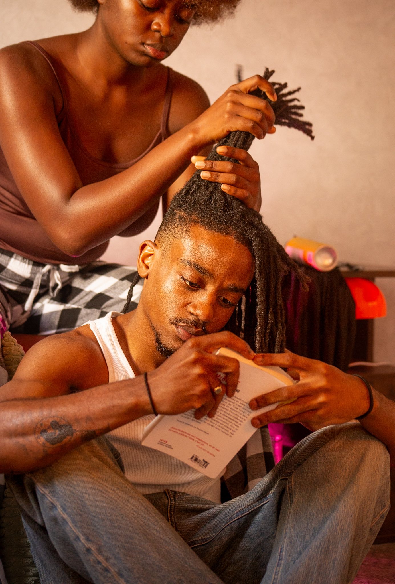 Portrait de couple : l'un lit, l'autre démêle ses locks, lumière chaude