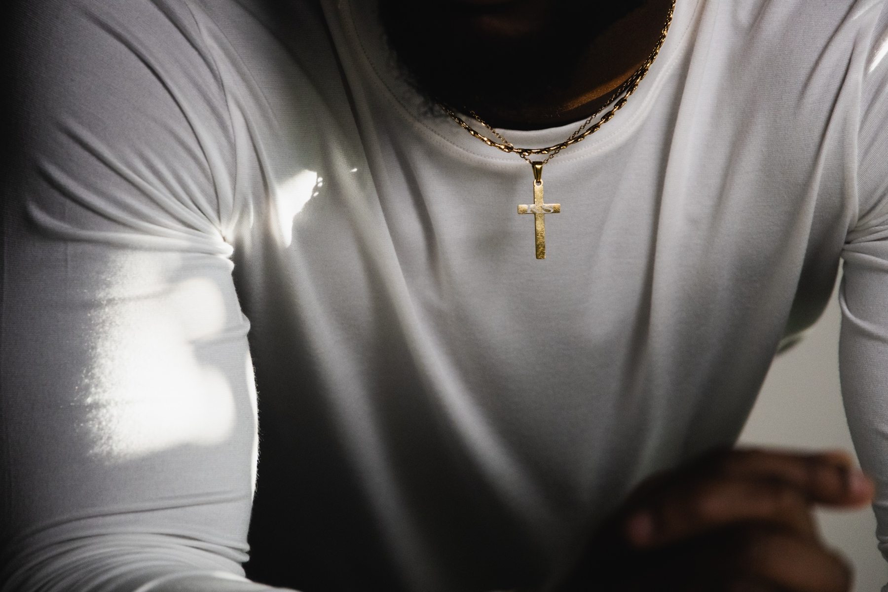 Détail : croix dorée gravée sur t-shirt blanc, reflet de lumière sur l'épaule