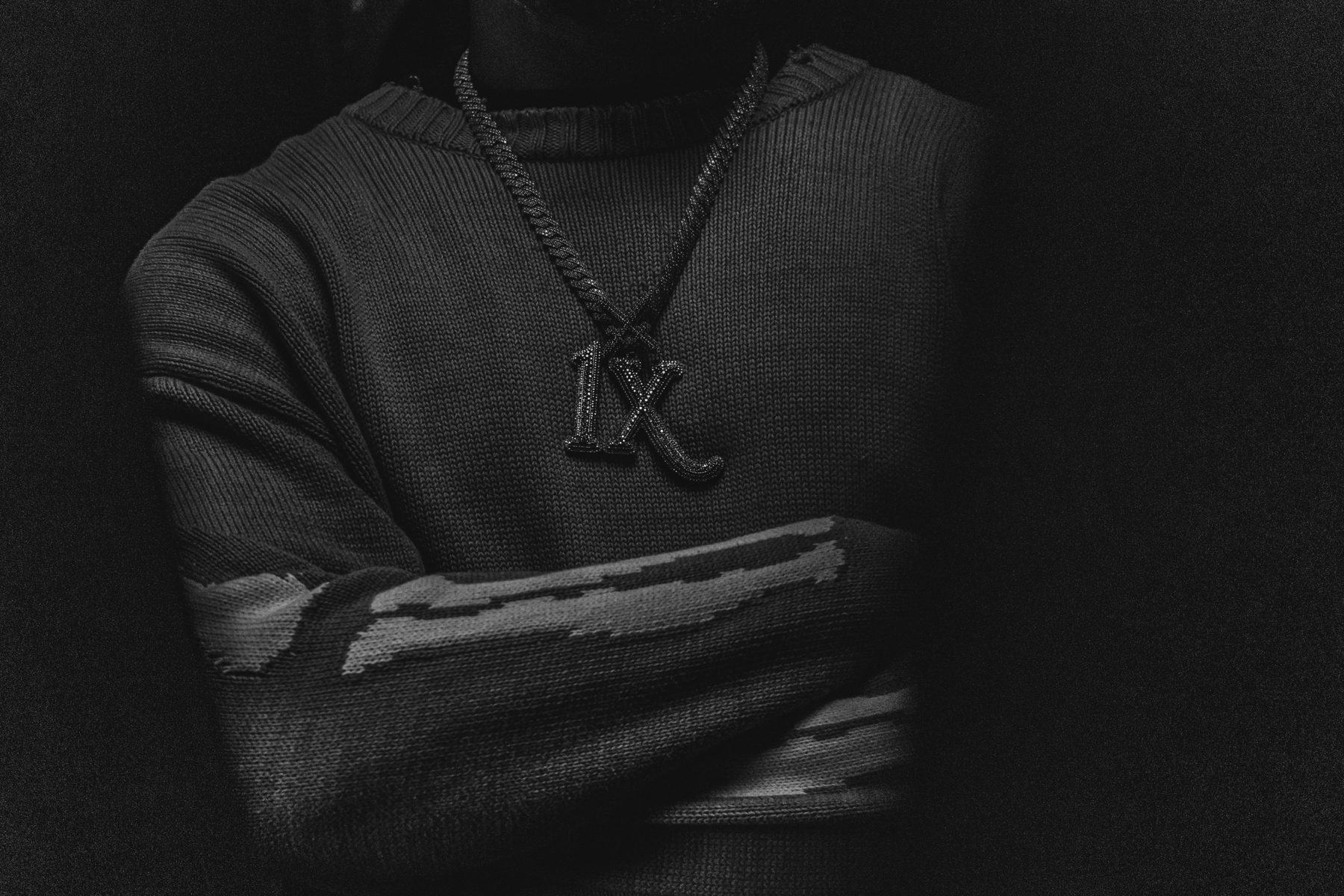 Détail : pendentif IX noir sur pull tricoté, bras croisés