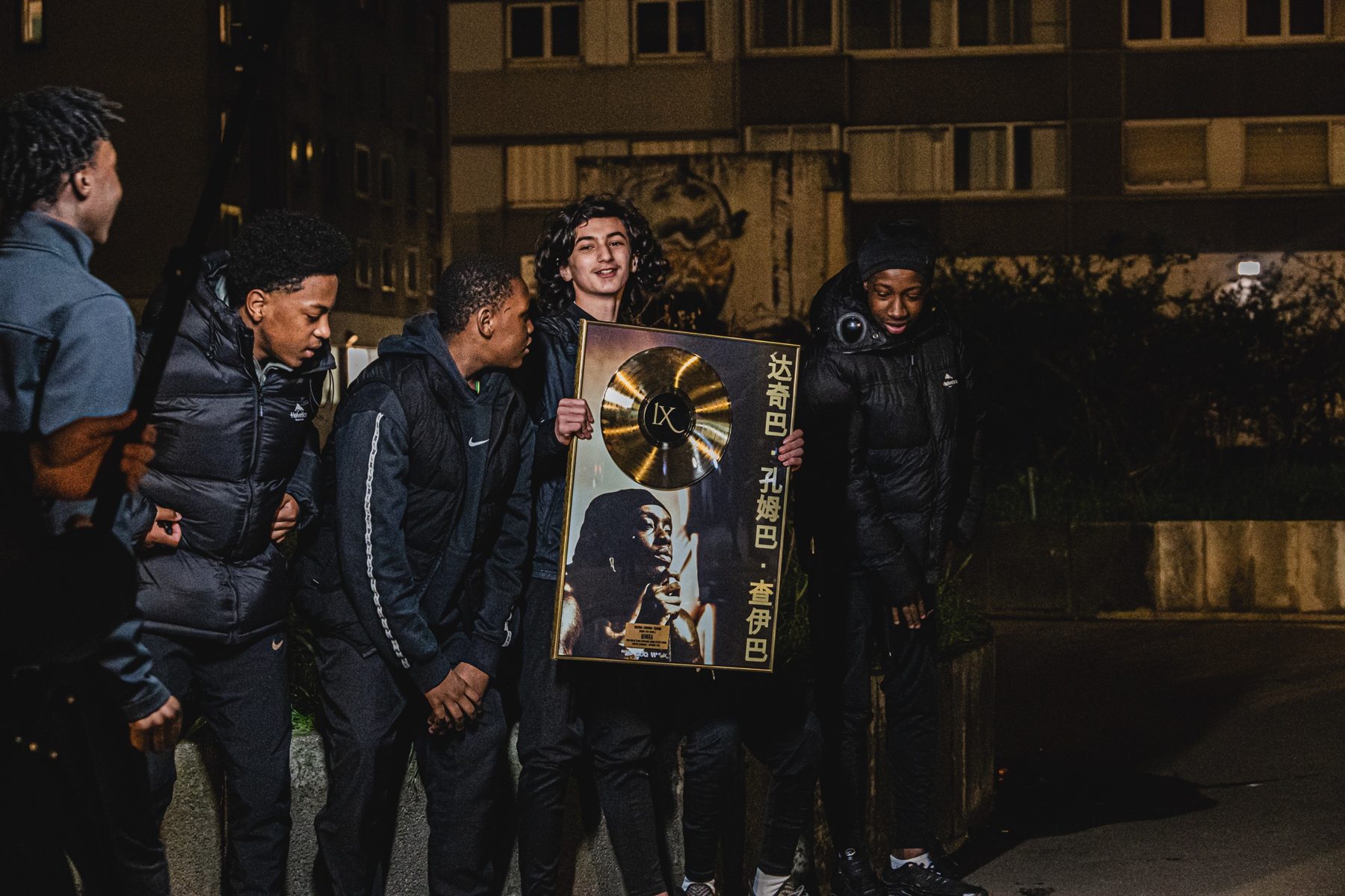 Remise du disque d'or : un jeune tient le cadre doré, ses amis rient autour de lui