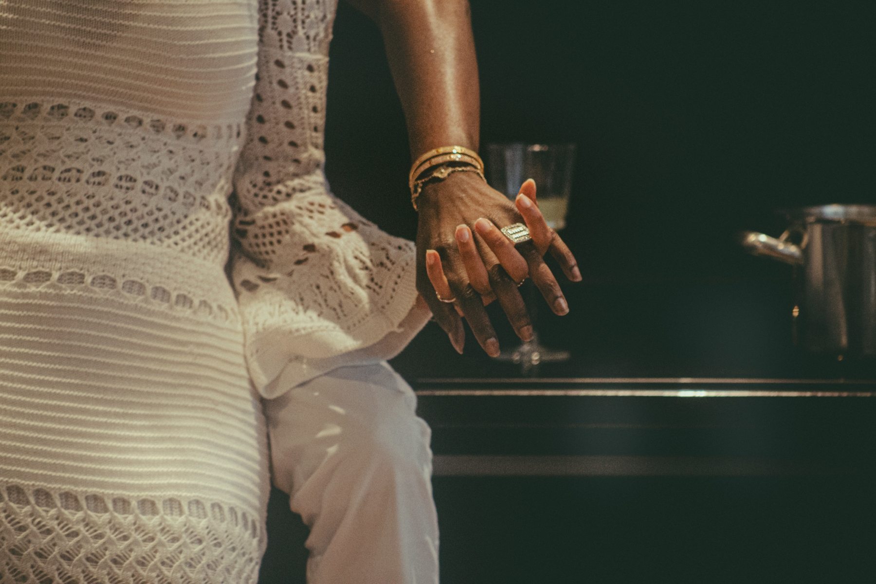 Détail d'une main aux bagues et bracelets dorés, tenue en maille ajourée blanche