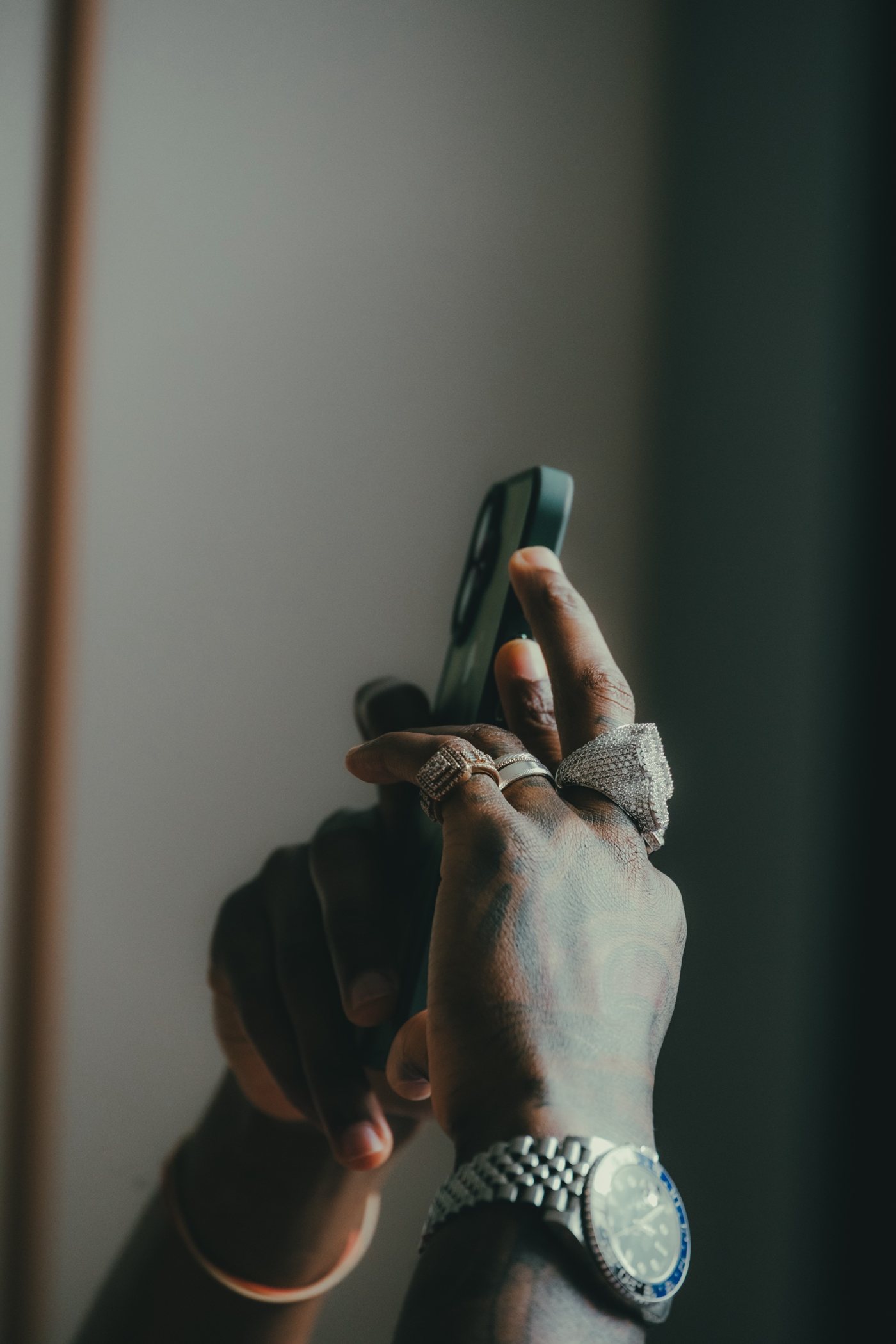 Gros plan sur les mains : bagues pavées, montre, téléphone vert
