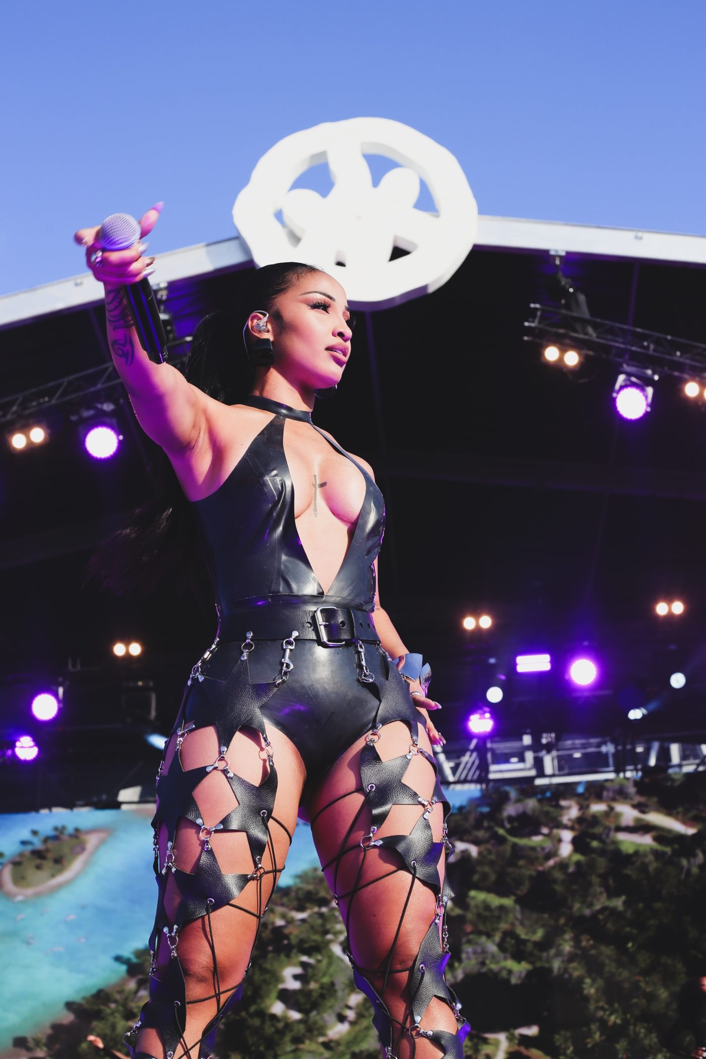 Chanteuse le bras tendu avec son micro sous un ciel bleu, tenue noire en latex