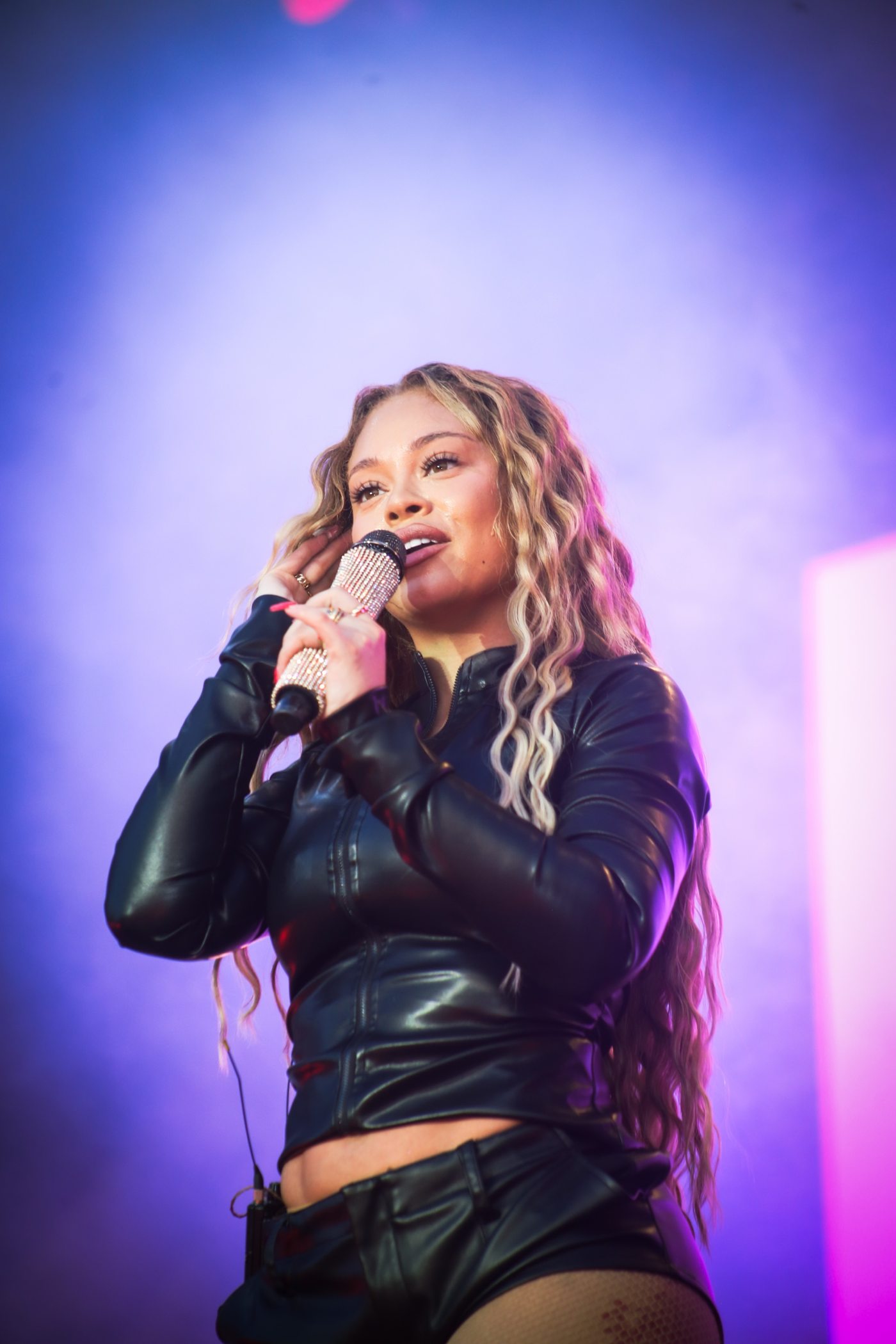 Chanteuse en veste de cuir noir dans une lumière violette, micro strassé