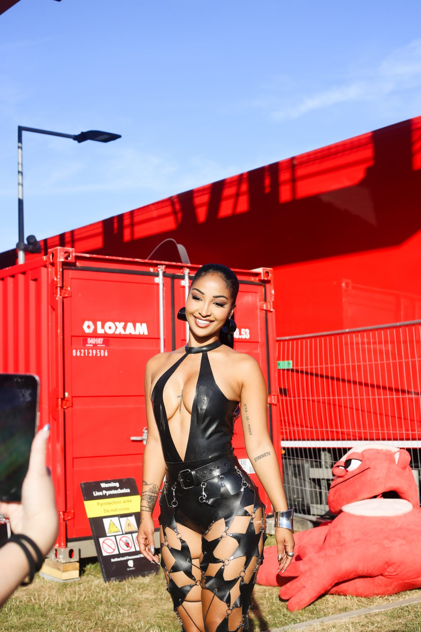 Chanteuse souriante devant un conteneur rouge, tenue noire en latex